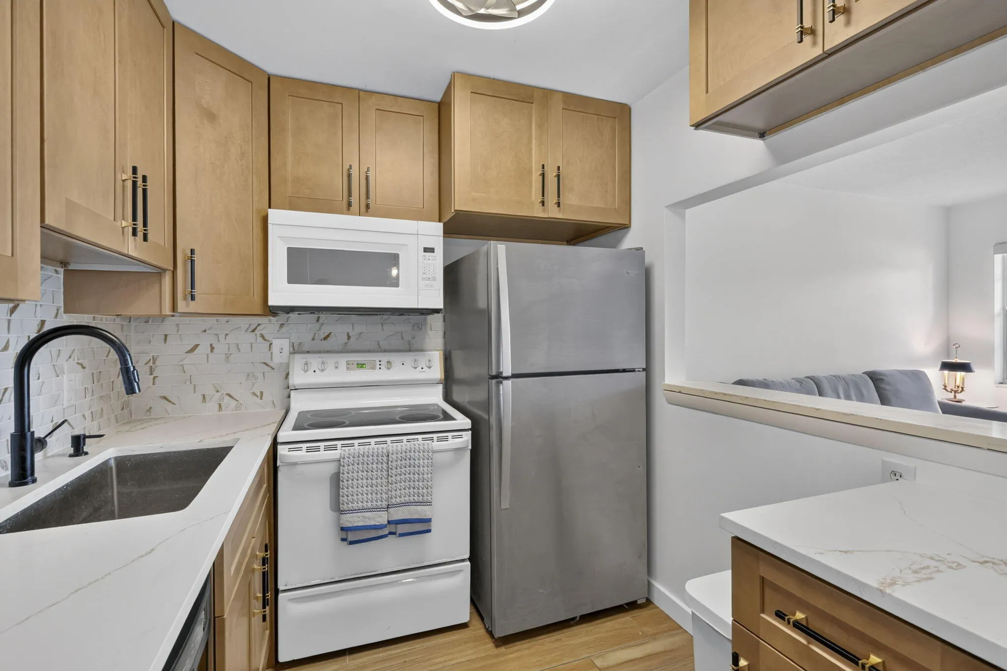 Kitchen featuring light wood-finish cabinetry, stainless steel refrigerator, white electric range, and an integrated stainless steel sink with a matte black faucet