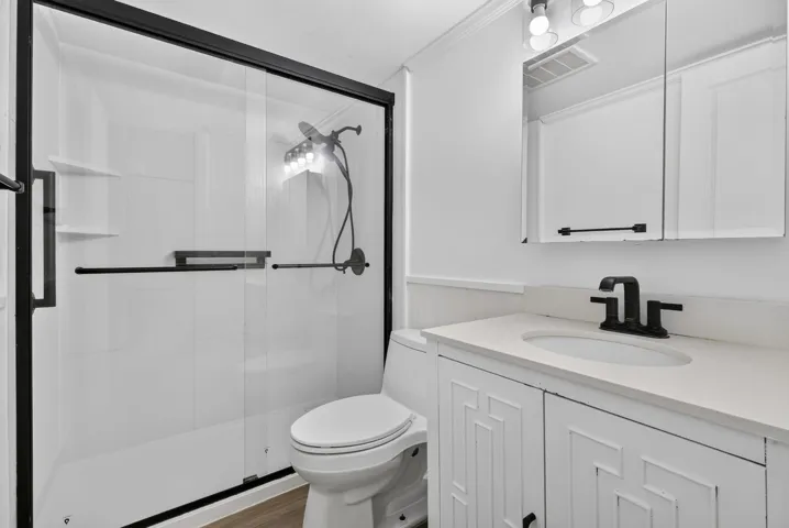 Bathroom featuring a glass-enclosed shower with black trim, a white vanity with paneled doors, a white countertop, and a black faucet
