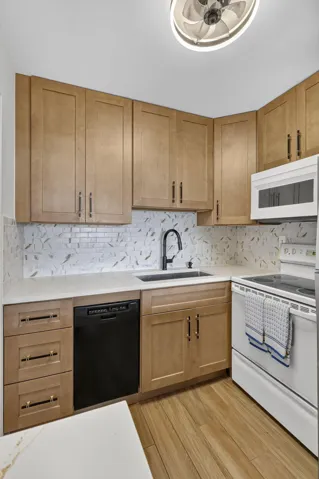 Modern kitchen featuring wood-finish cabinetry, white countertops, a tiled backsplash, and wood-finish flooring