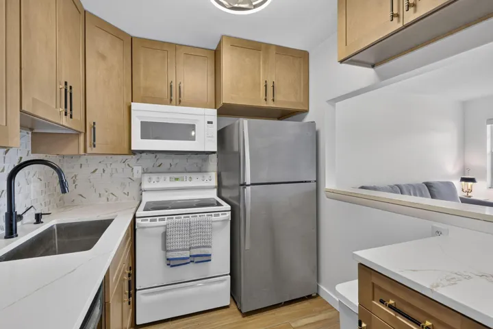 Kitchen featuring light wood-finish cabinetry, stainless steel refrigerator, white electric range, and an integrated stainless steel sink with a matte black faucet