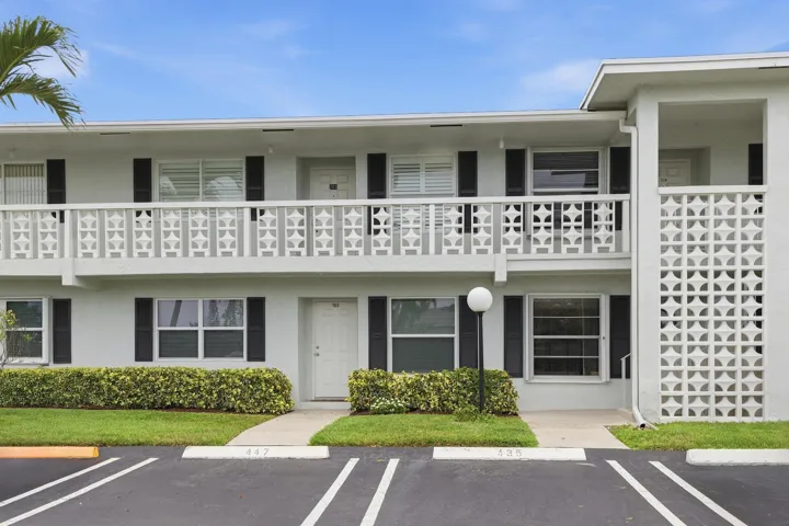 Two-story building featuring a decorative balcony railing, horizontal window shutters, a prominent decorative screen wall, and a well-maintained shrub border