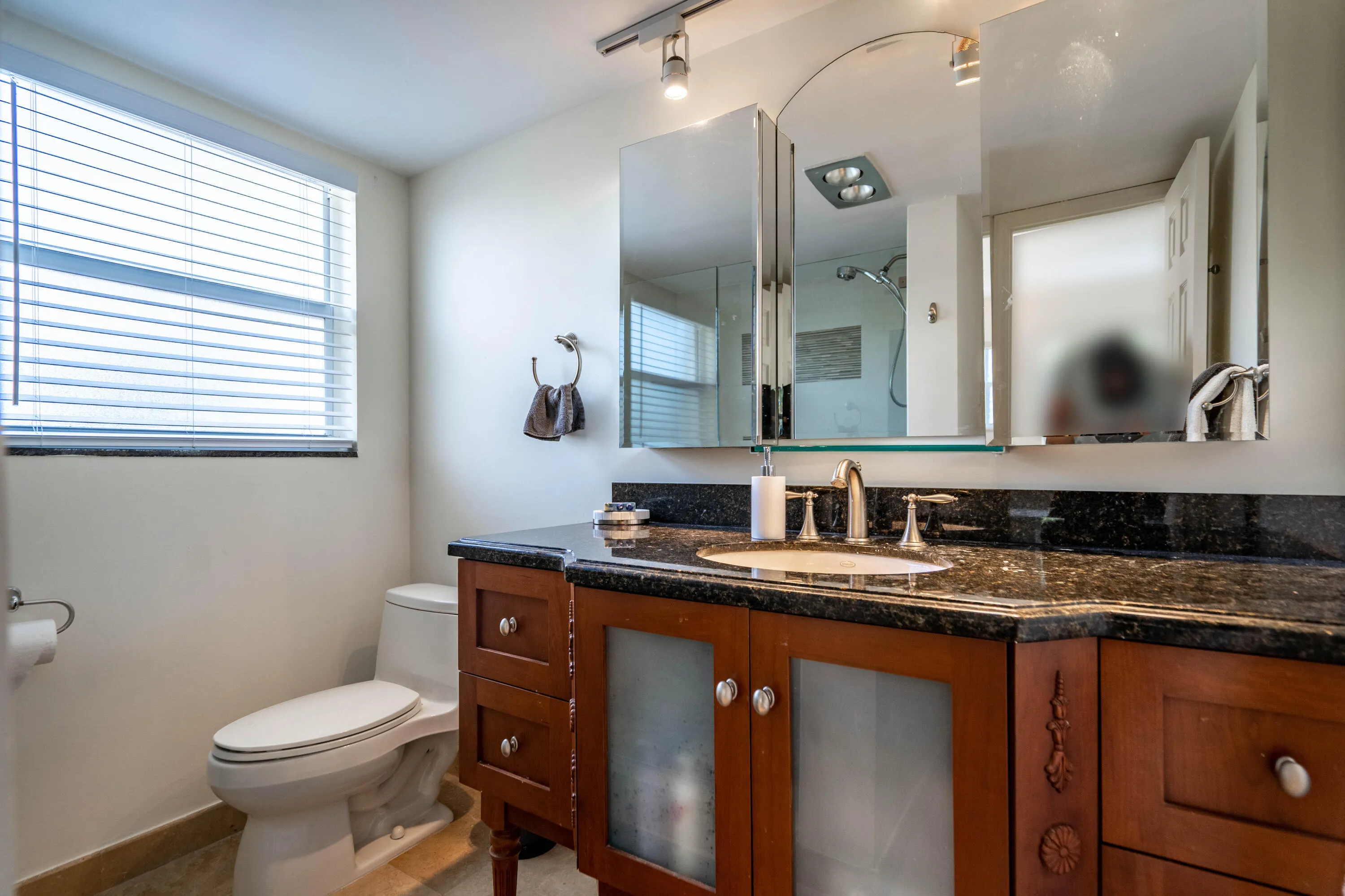 Rich wood-finish vanity with a built-in sink, dark speckled countertop, and mirrored medicine cabinet