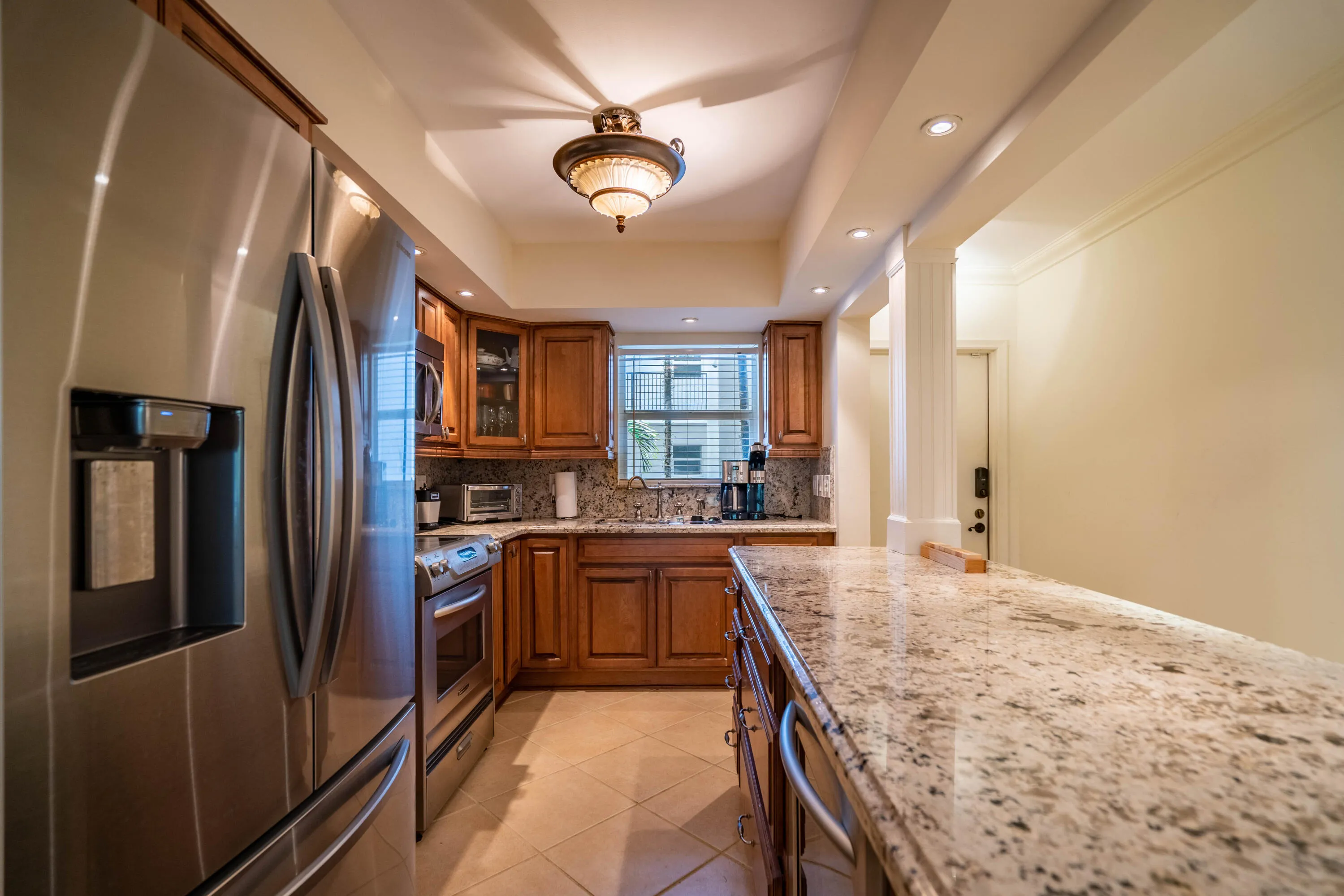 Stainless steel refrigerator, granite countertops, tile flooring, wood cabinetry, and recessed lighting