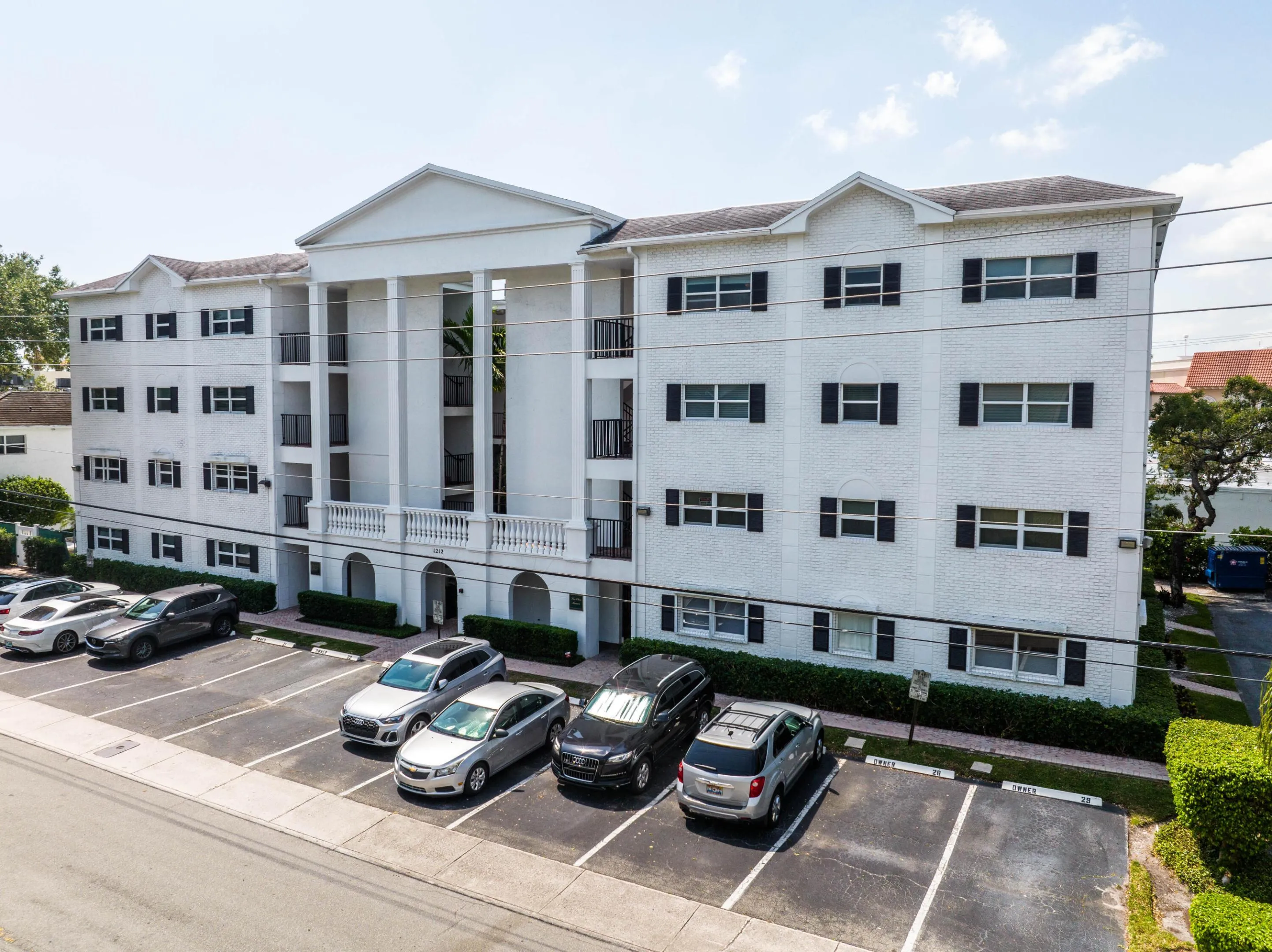 White stucco exterior with black shutters, prominent portico entrance with columns, multiple balconies with black railings, and an on-site parking lot