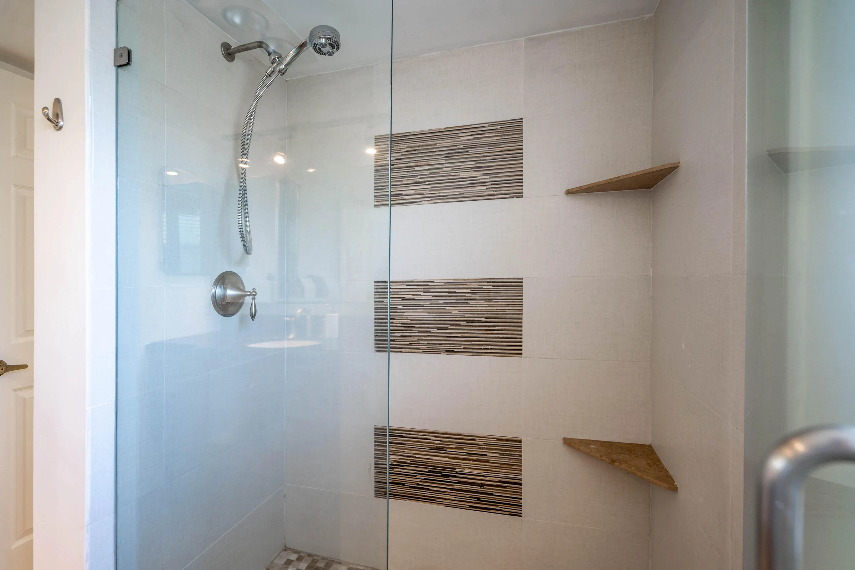 Glass-enclosed shower with a brushed nickel shower head and control