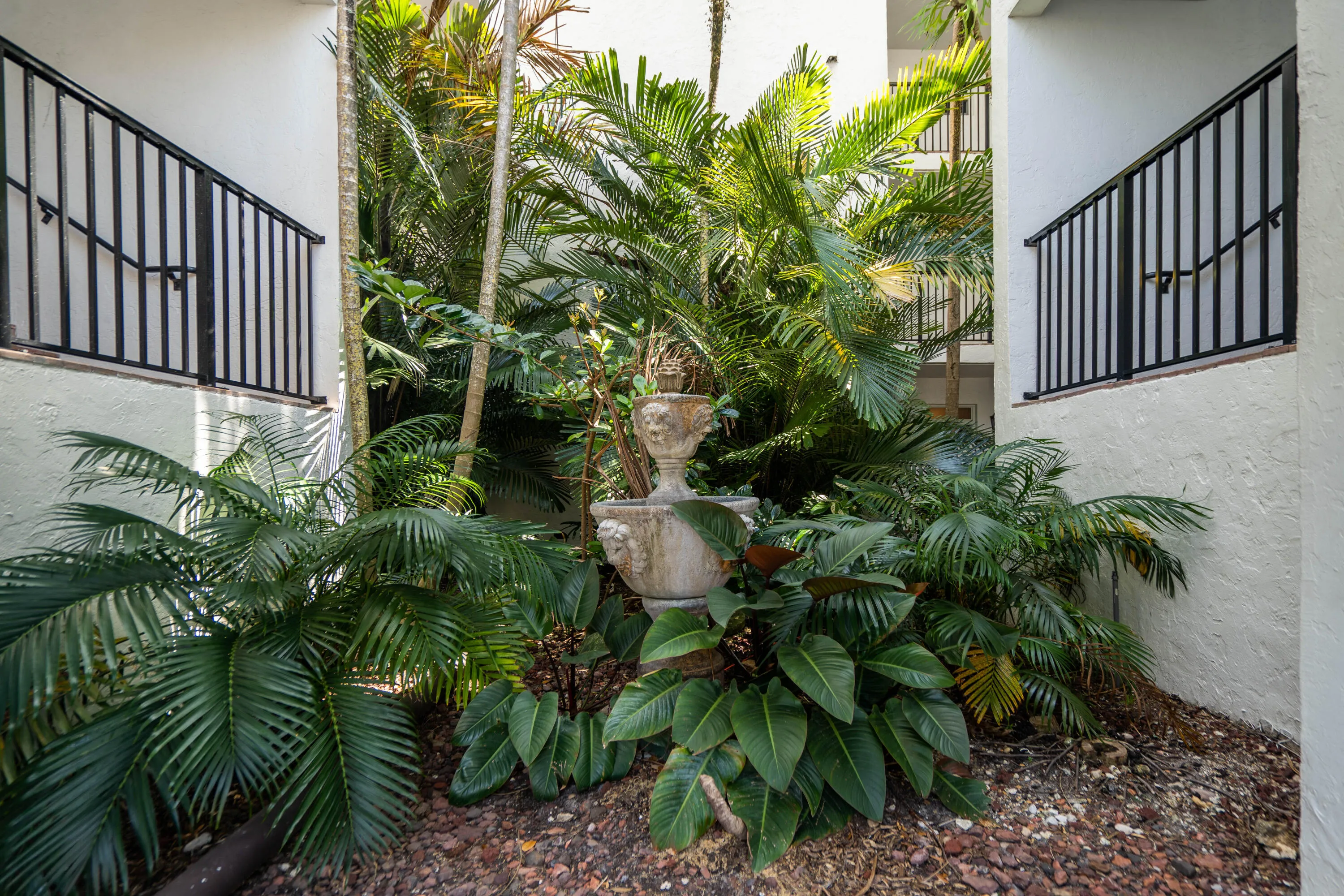 Courtyard featuring lush tropical landscaping, a decorative stone fountain, and architectural balconies with black railings