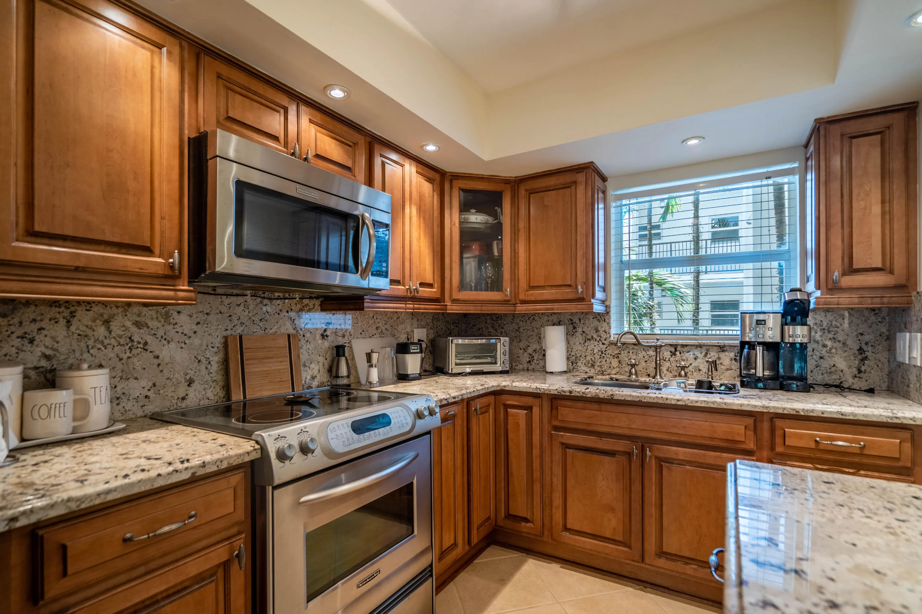 Hardwood cabinetry with stainless steel appliances, granite countertops, and a full-height granite backsplash