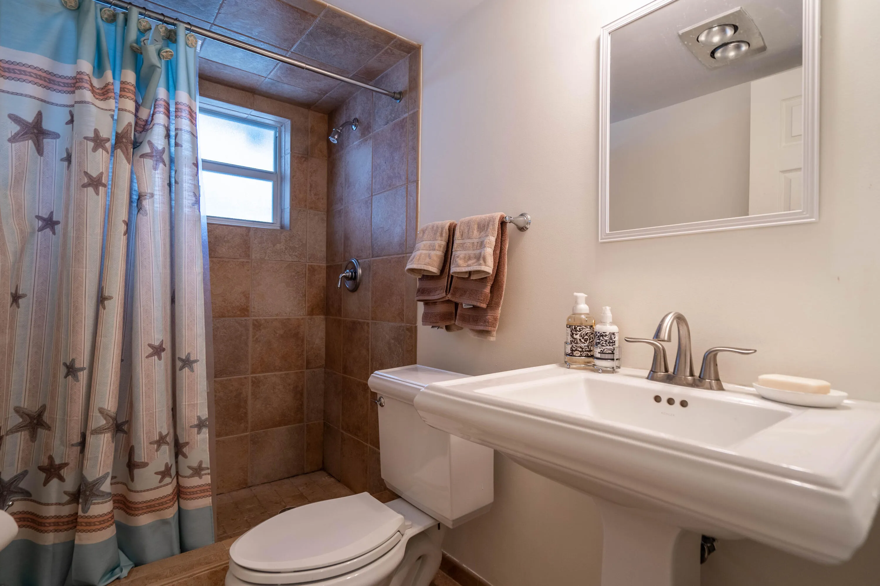 Pedestal sink with brushed nickel faucet, framed wall mirror, tile flooring, and tiled shower surround with window