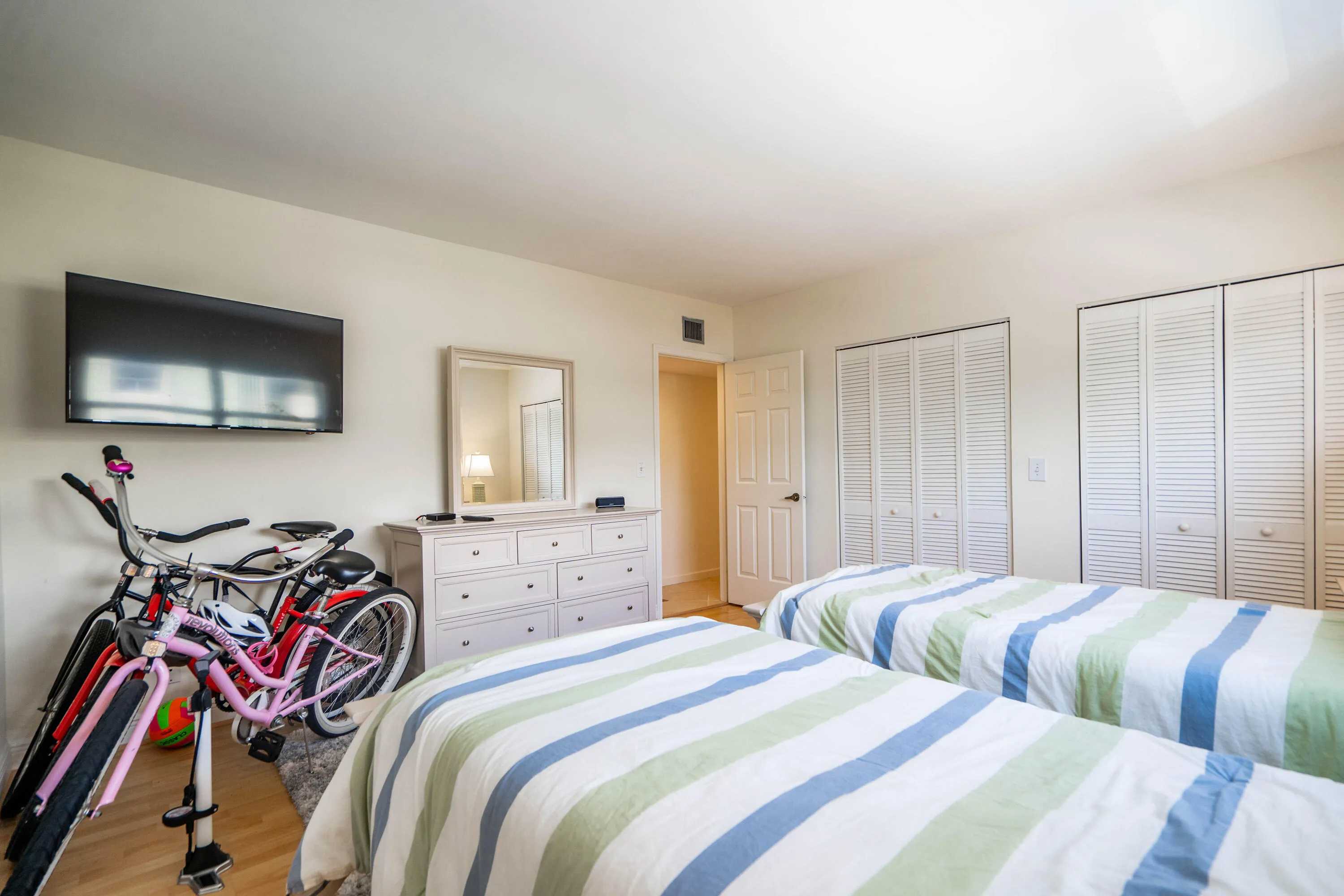 Wall-mounted television with white louvered closet doors, a neutral wall color, and wood-finish flooring