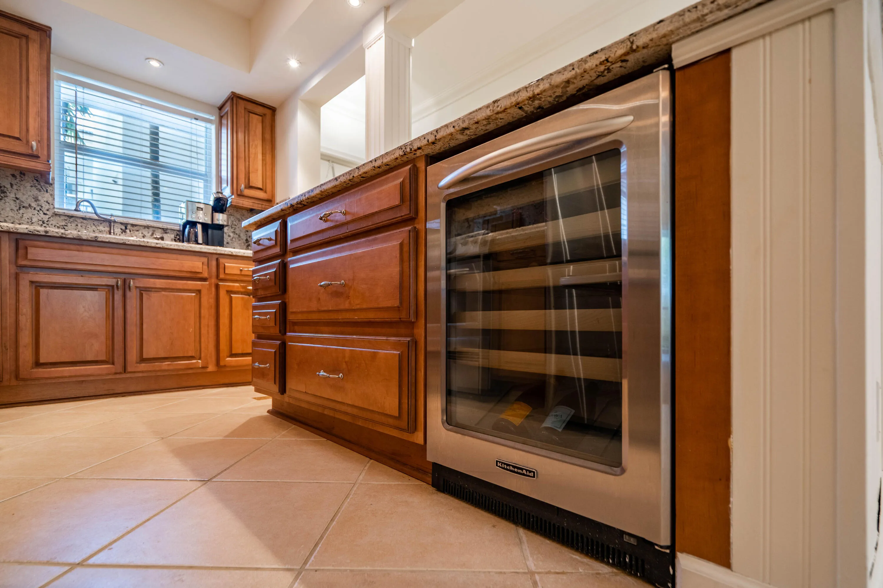 Kitchen featuring wood cabinetry, stone countertops, integrated stainless steel beverage cooler, recessed lighting, and tile flooring