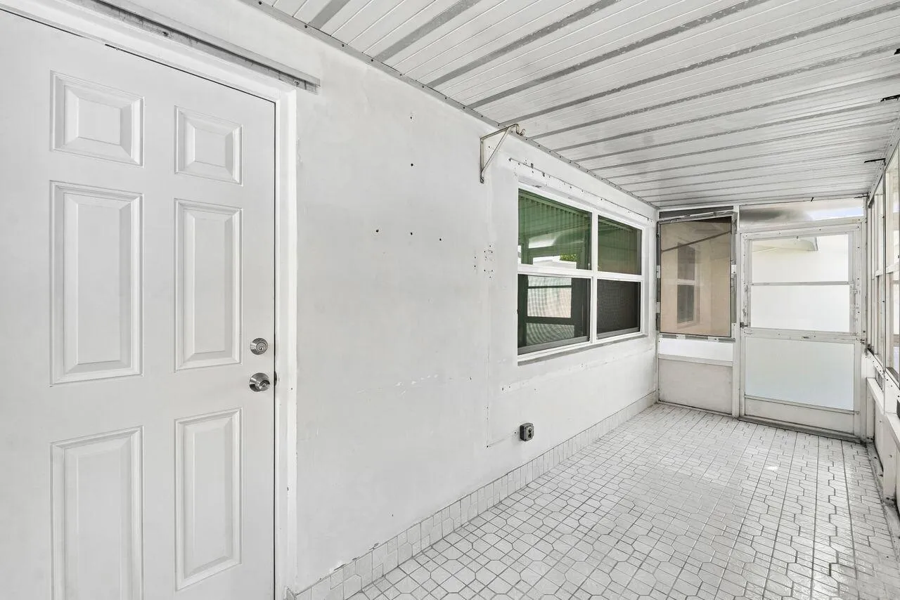 Enclosed patio featuring a white paneled door, multiple windows, a screened door, and patterned tile flooring