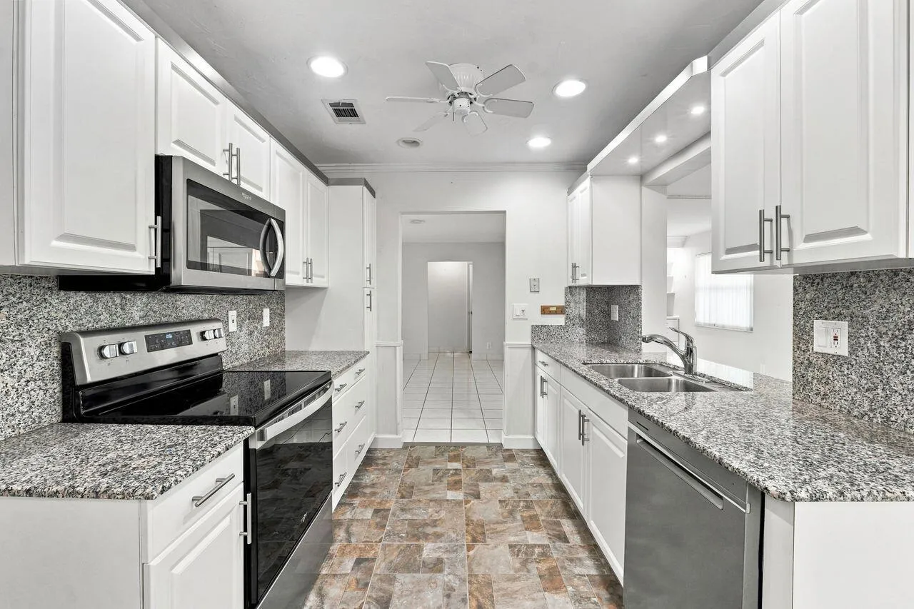 Galley kitchen with white cabinetry, granite countertops, stainless steel appliances, and ceiling fan
