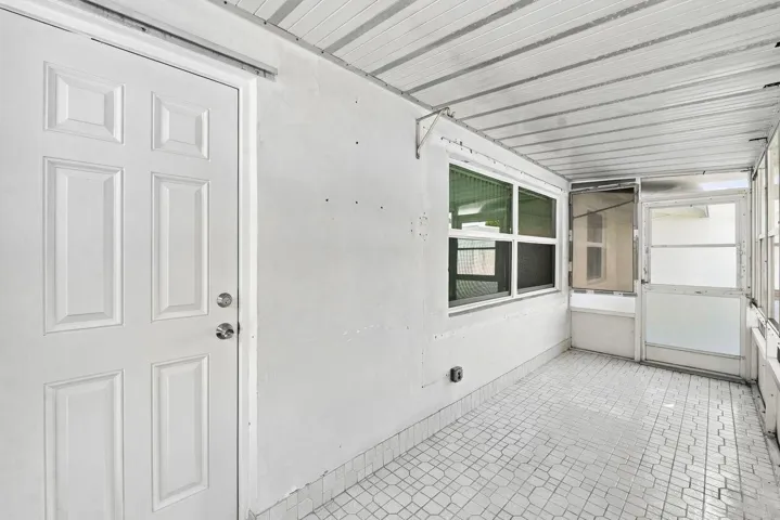 Enclosed patio featuring a white paneled door, multiple windows, a screened door, and patterned tile flooring