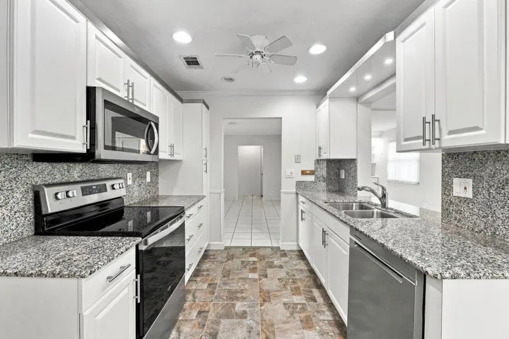 Galley kitchen with white cabinetry, granite countertops, stainless steel appliances, and ceiling fan