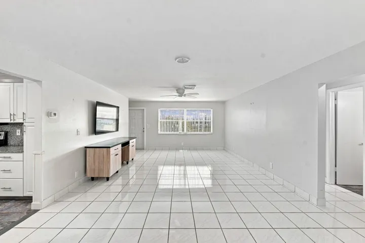 Expansive open-concept living area featuring white tile flooring, light and bright with a custom TV cabinet and wall mounted TV