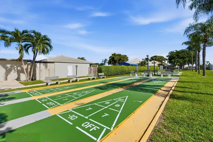 Community shuffleboard courts with multiple lanes, surrounded by mature palm trees and lush green landscaping