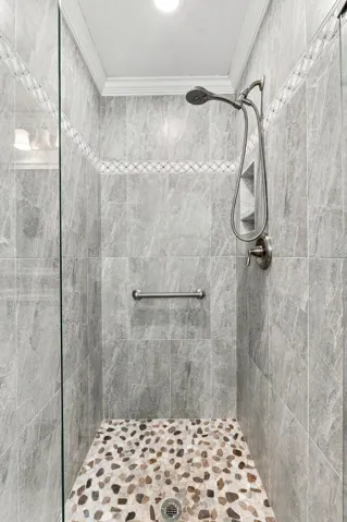 Glass-enclosed shower featuring large format tile walls, decorative accent tile, a built-in shower niche, and a pebble-tiled floor