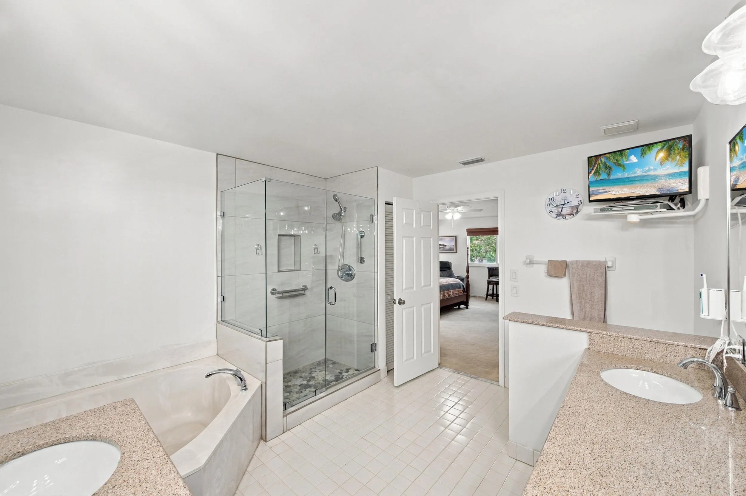Spacious bathroom featuring a glass-enclosed shower, built-in bathtub, and dual vanity with integrated sinks and stone-finish countertops