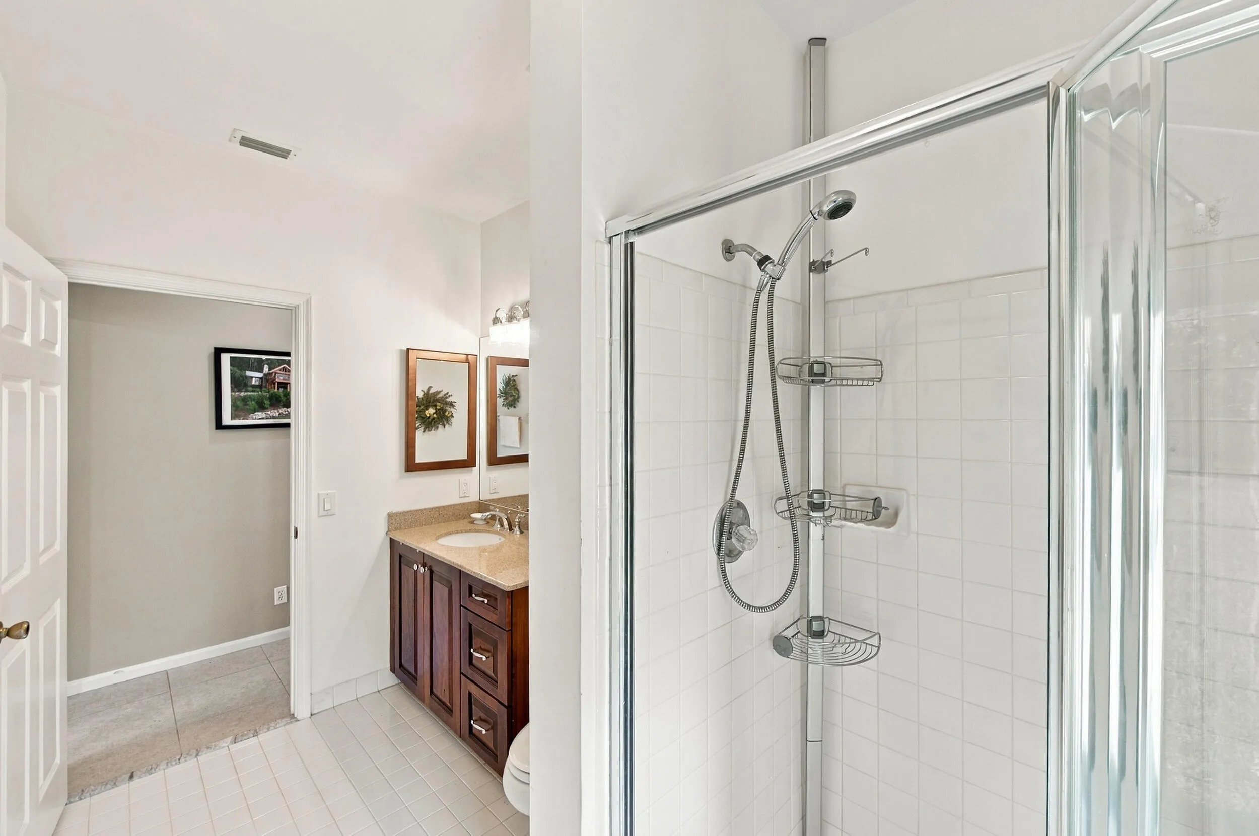 Glass-enclosed shower with white tiled walls, wood-finish vanity with countertop, and a single sink with a dual-light fixture