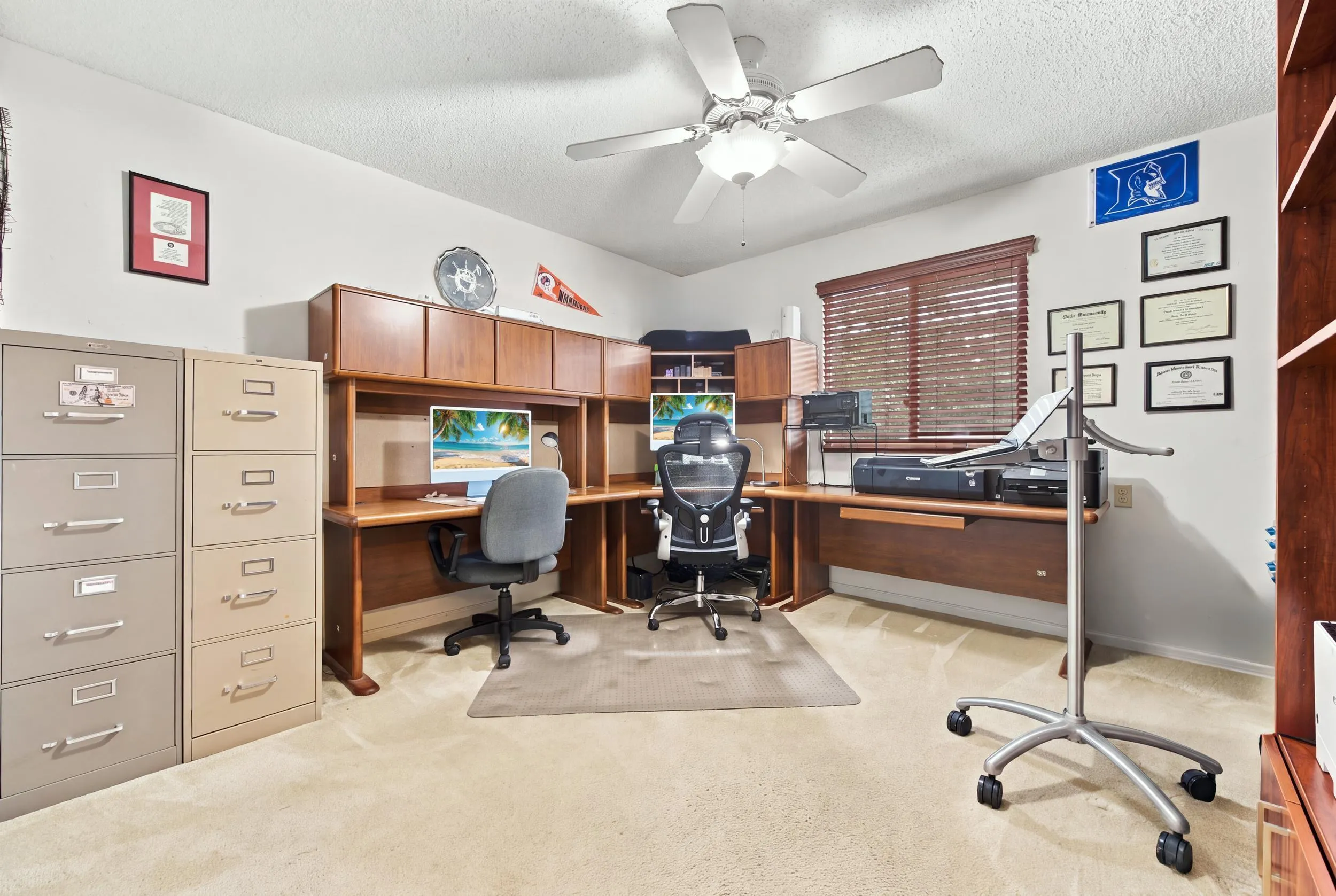 Built-in wooden desk with integrated cabinetry, window with wooden blinds, and ceiling fan with integrated lighting