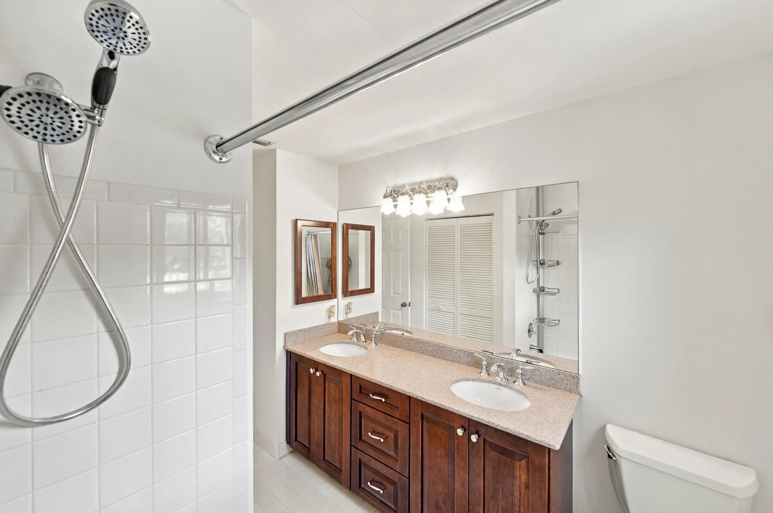 Dual vanity with undermount sinks, wood-finish cabinetry, and a full-width mirror