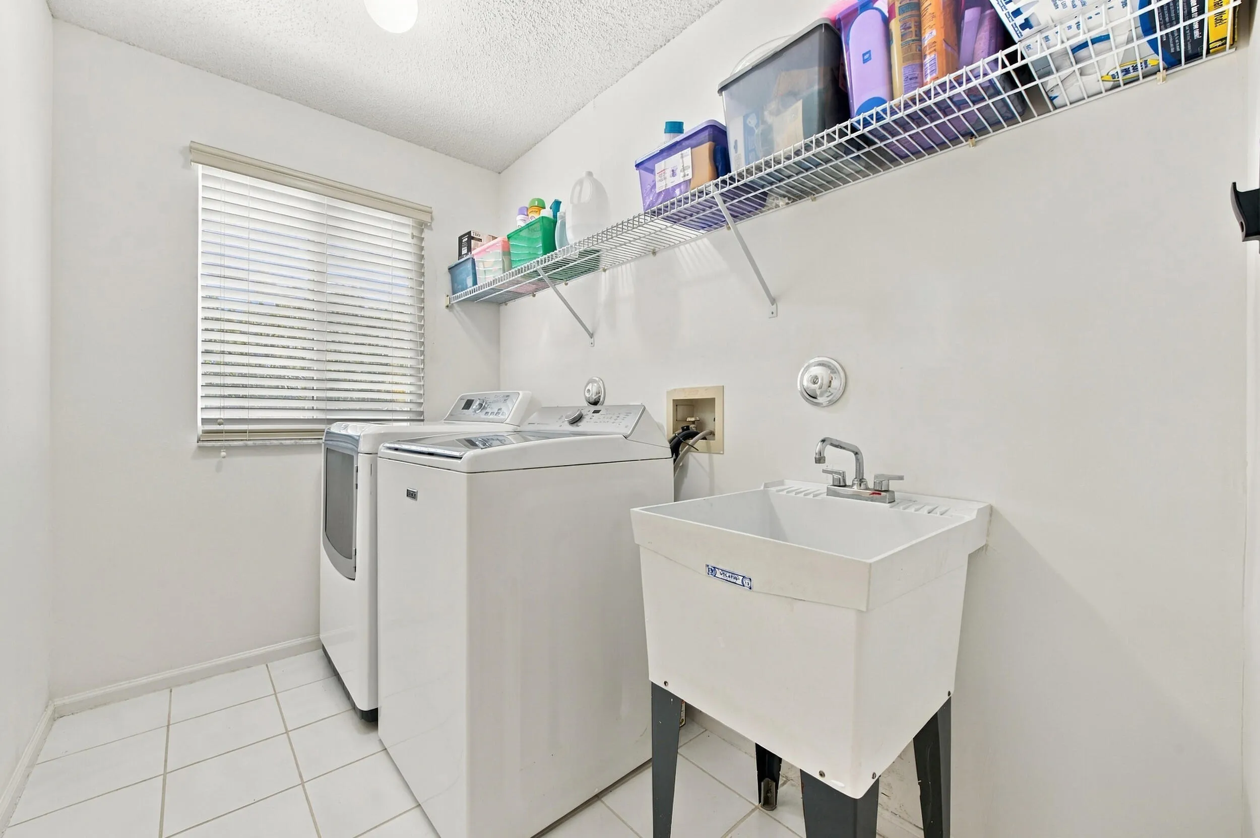 Dedicated laundry room featuring tile flooring, a utility sink, and wall-mounted wire shelving