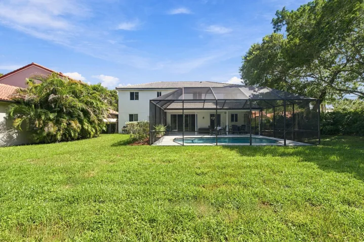 Expansive backyard featuring a screened pool enclosure, paved patio, and mature landscaping
