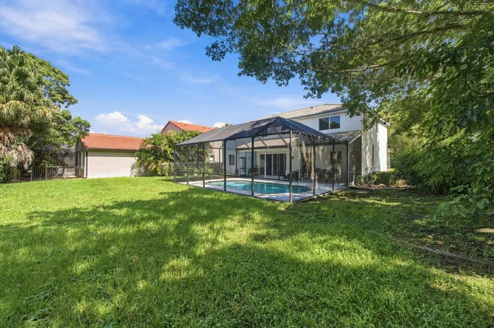 Expansive backyard with a screened pool enclosure, mature trees, and a two-story residence featuring multiple windows and a covered patio