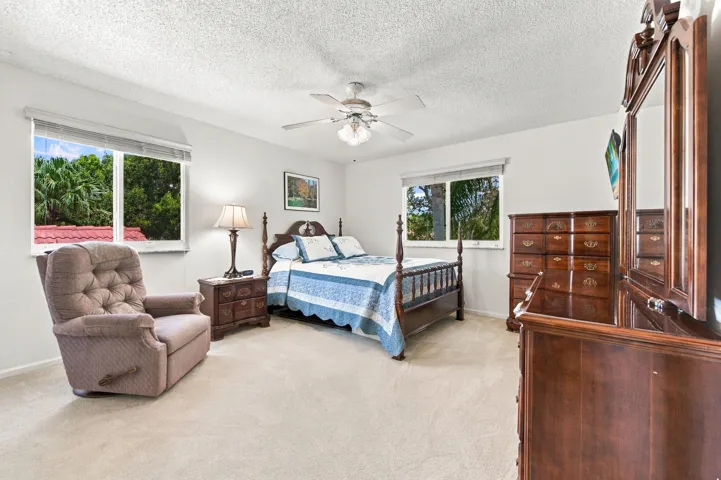 Textured ceiling, ceiling fan with integrated lighting, two windows with blinds, and light-colored carpeting