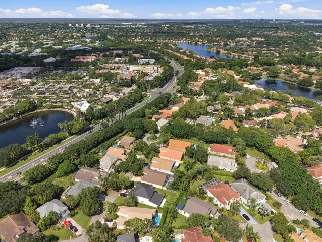 Aerial perspective showcasing a residential area with varied rooflines, abundant mature trees, multiple water features including lakes with fountains, and an extensive road network