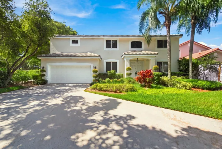 Stucco exterior with a tiled roof, mature tropical landscaping, a portico entrance, and a two-car garage