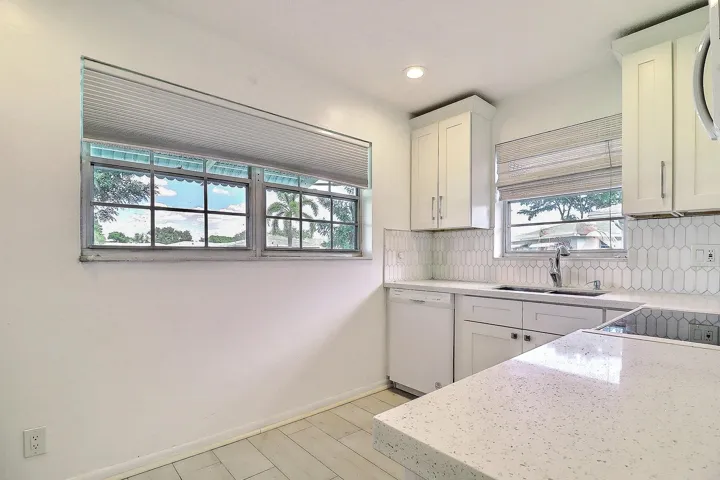 White shaker cabinetry, light-toned countertops, white subway tile backsplash, stainless steel sink with a gooseneck faucet, and integrated dishwasher