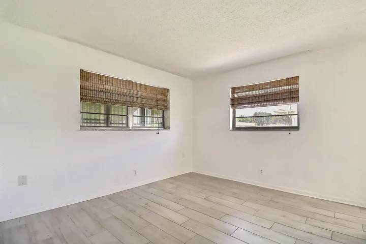 White walls with two large windows featuring woven blinds, wood-finish plank flooring, and a textured ceiling