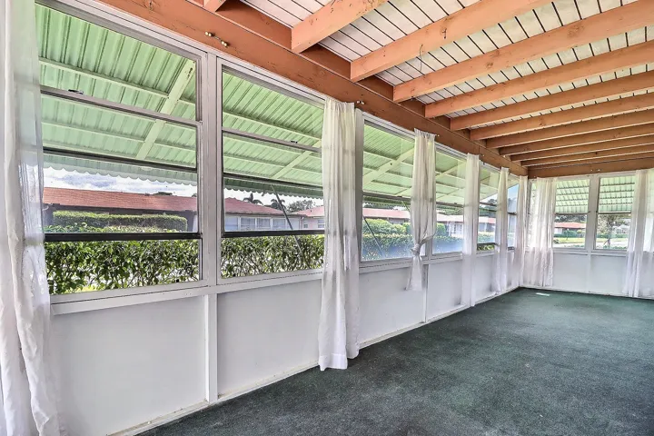 Screened enclosure with an exposed wood beam ceiling, multiple awning windows, and a green carpeted floor