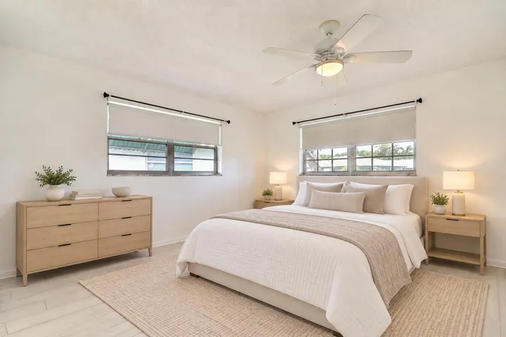 White ceiling fan with integrated lighting, two windows with roller shades, and light wood-finish flooring