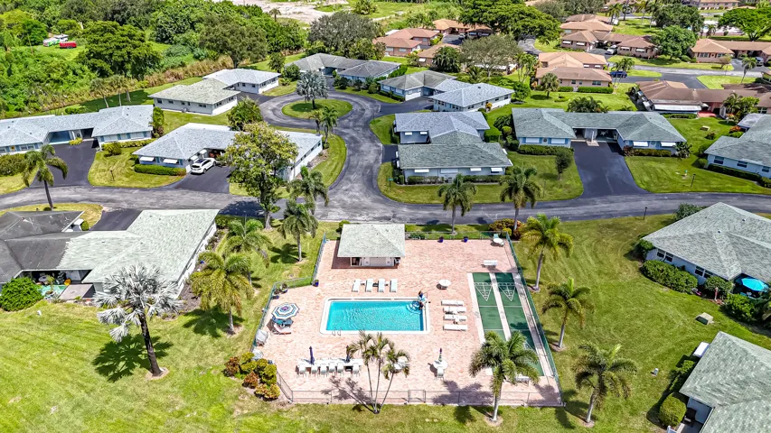 Community setting featuring a central swimming pool, paved pool deck, shuffleboard courts, mature palm trees, and single-story residences