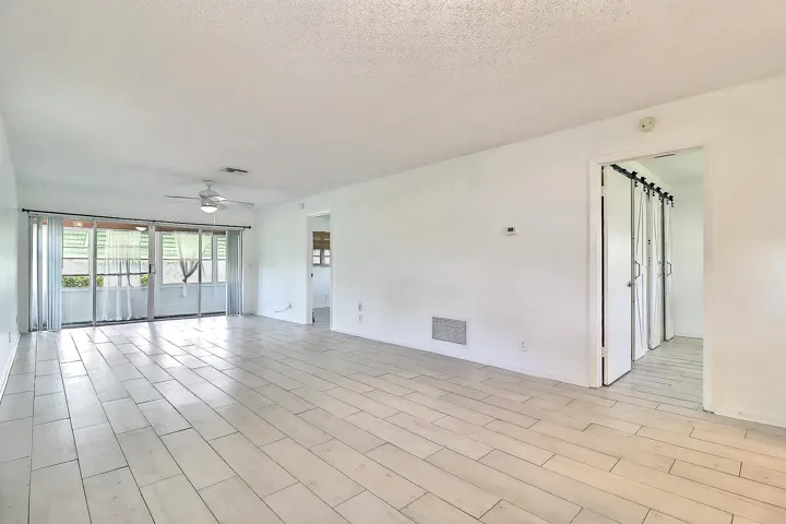 Spacious living area featuring light-toned tile flooring, white walls, and a ceiling fan