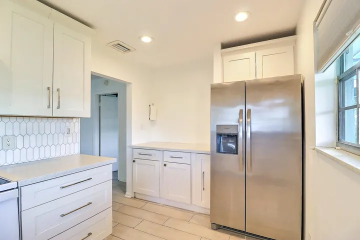 White shaker cabinetry, light-toned countertops, geometric tile backsplash, recessed lighting, and stainless steel refrigerator