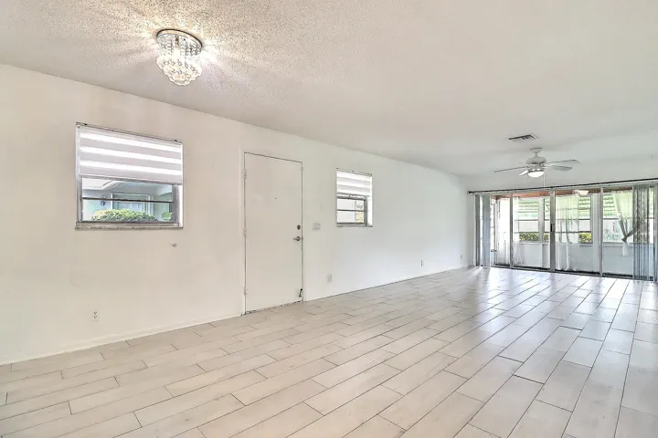 Expansive living space featuring wood-finish tile flooring, a crystal flush mount ceiling light, and a ceiling fan with integrated lighting