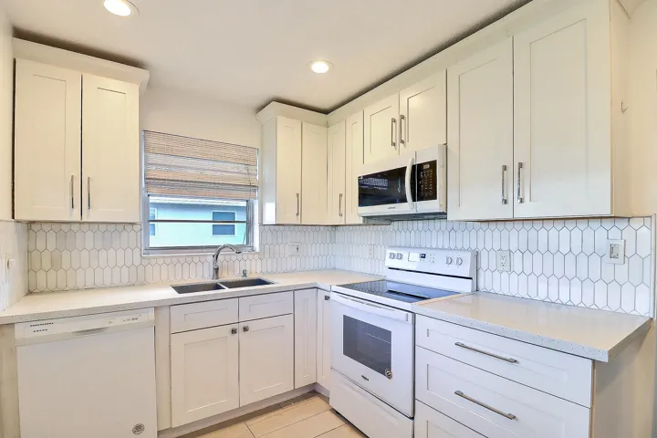 White shaker cabinetry with bar pulls, white appliance package, solid surface countertops, dual basin stainless steel sink, and a picket tile backsplash