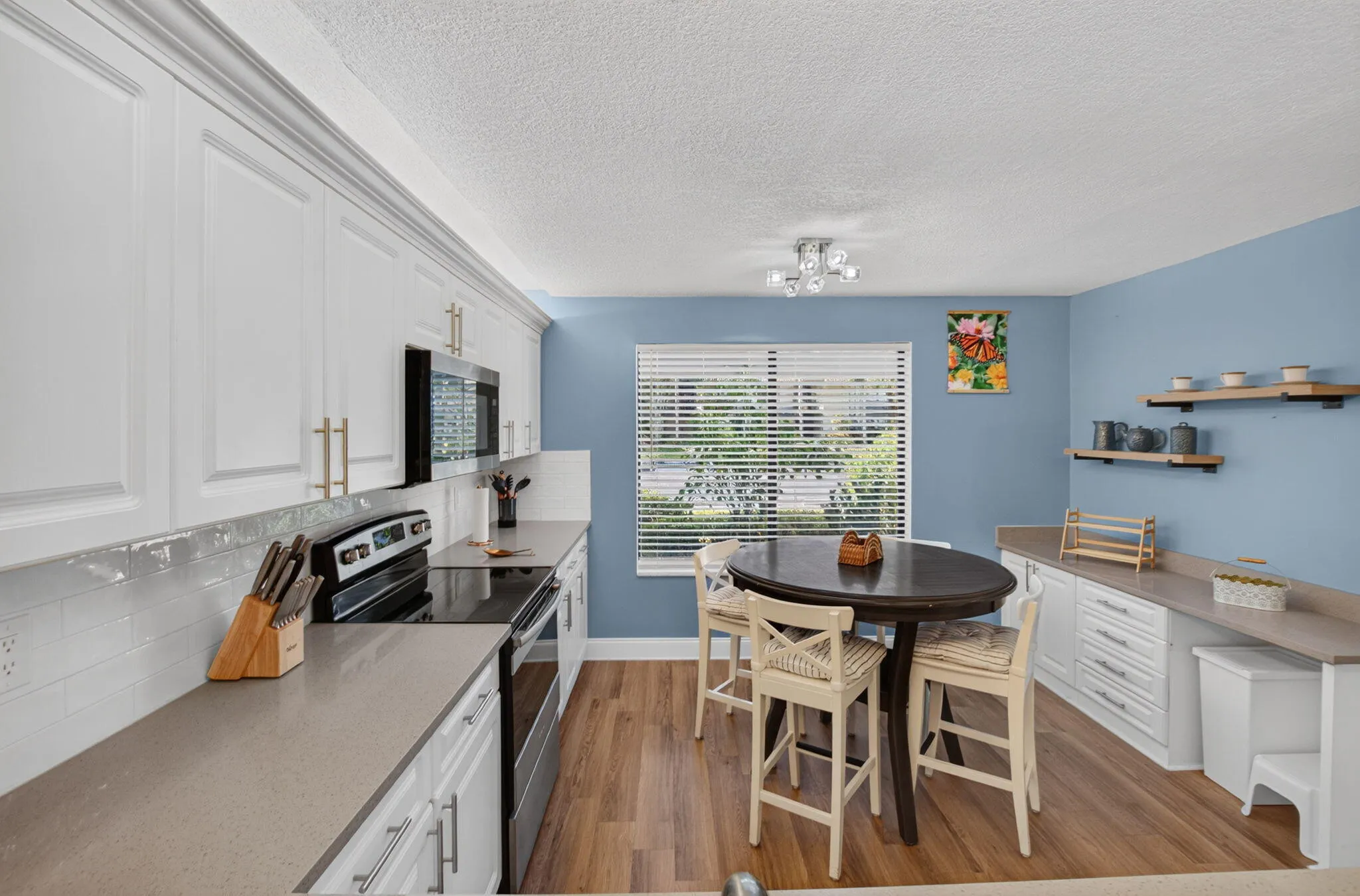 White upper and lower cabinetry, quartz countertops, wood-finish flooring, and white subway tile backsplash