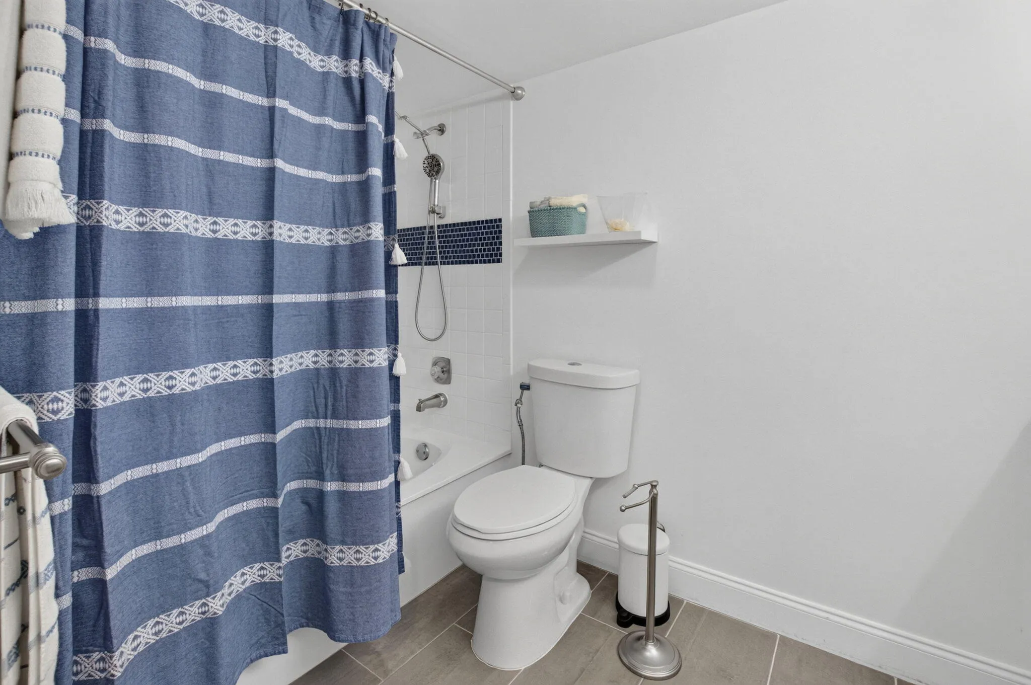 Bathtub with subway tile surround and mosaic accent, white toilet, and tile flooring
