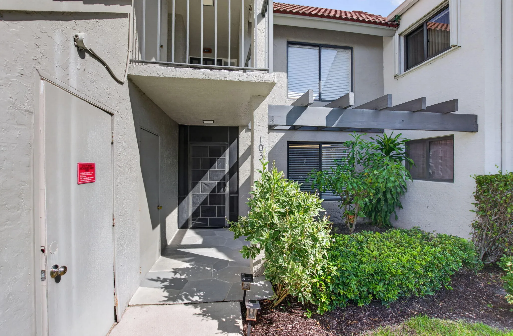 Exterior entrance with screen door, stone tile walkway, and an overhead pergola feature