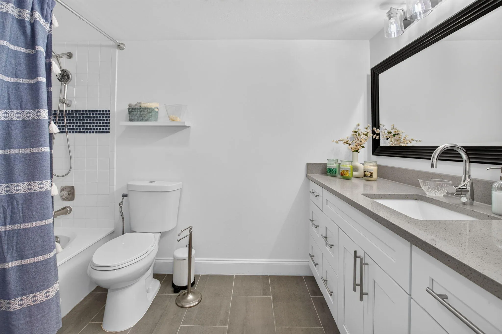 White bath vanity with a grey countertop, framed mirror, and tile flooring