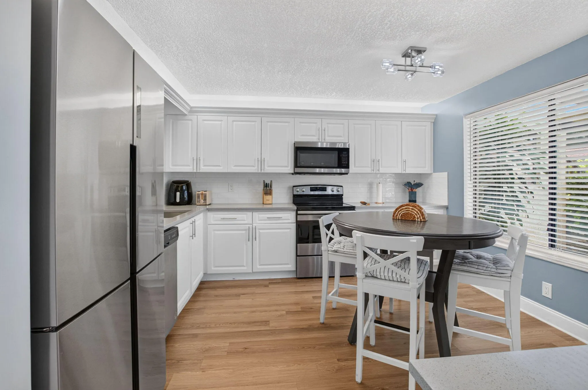 Kitchen featuring white shaker cabinetry, stainless steel appliances, wood-finish flooring, and a white subway tile backsplash
