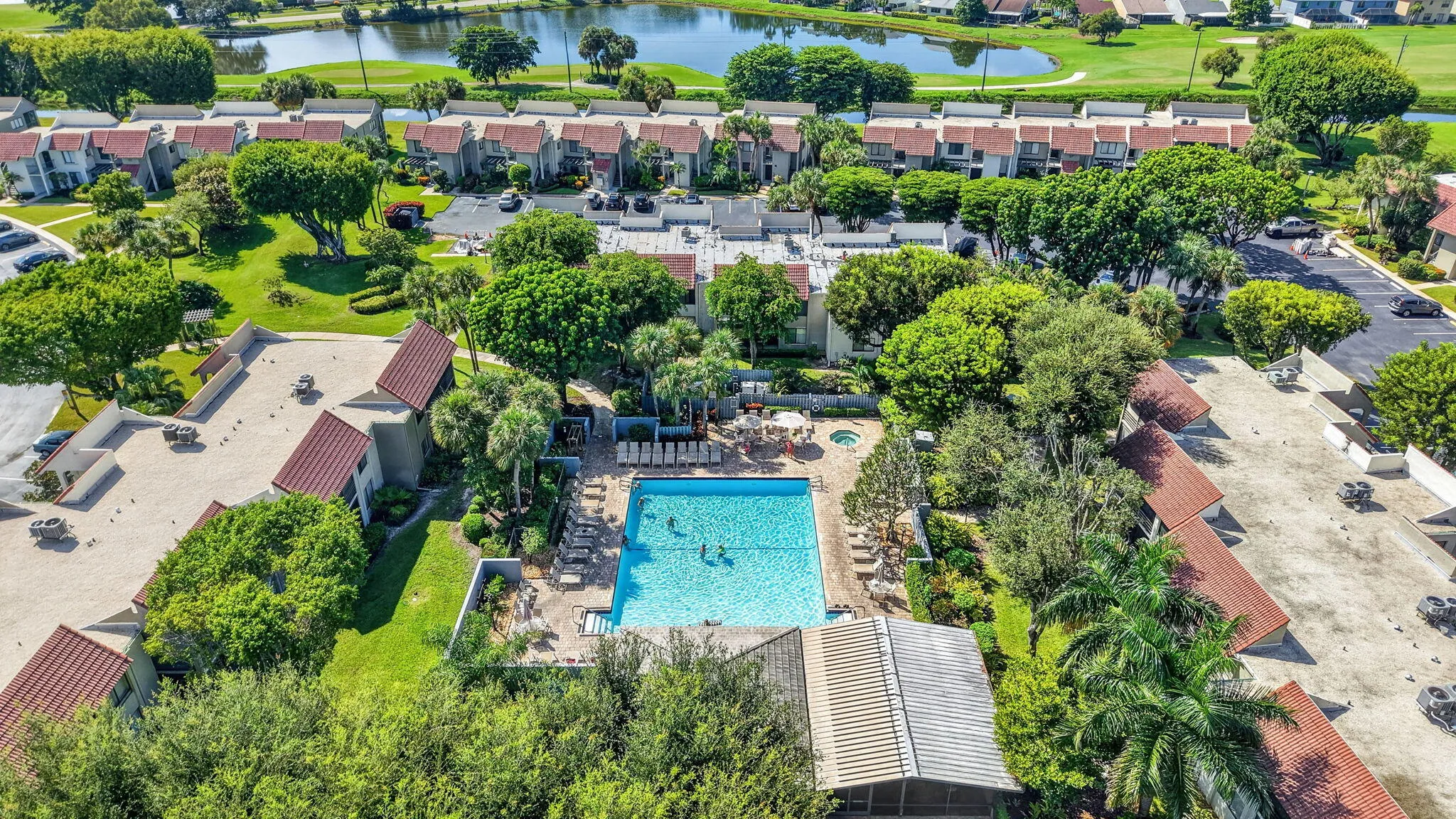 Community pool with surrounding lounge seating, hot tub, and mature landscaping
