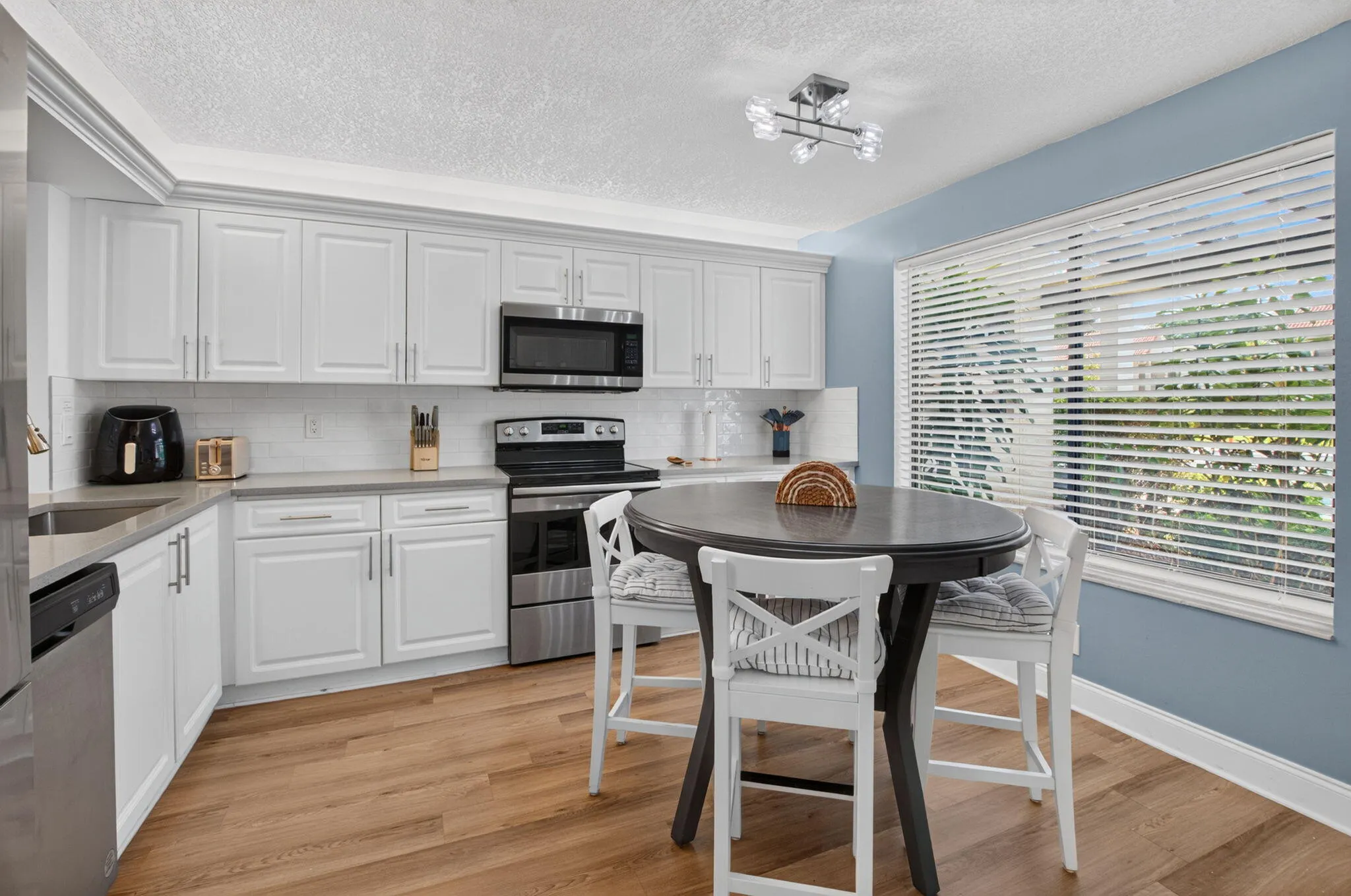 Modern kitchen featuring white shaker cabinetry, stainless steel appliances, wood-finish flooring, and sunlight!