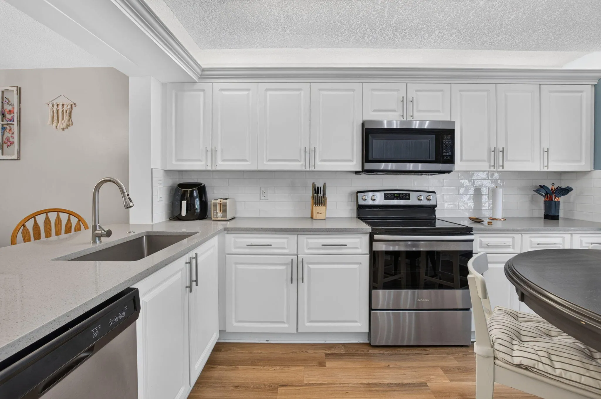 White shaker-style cabinetry, stainless steel appliances, quartz countertops, subway tile backsplash, and wood-finish flooring