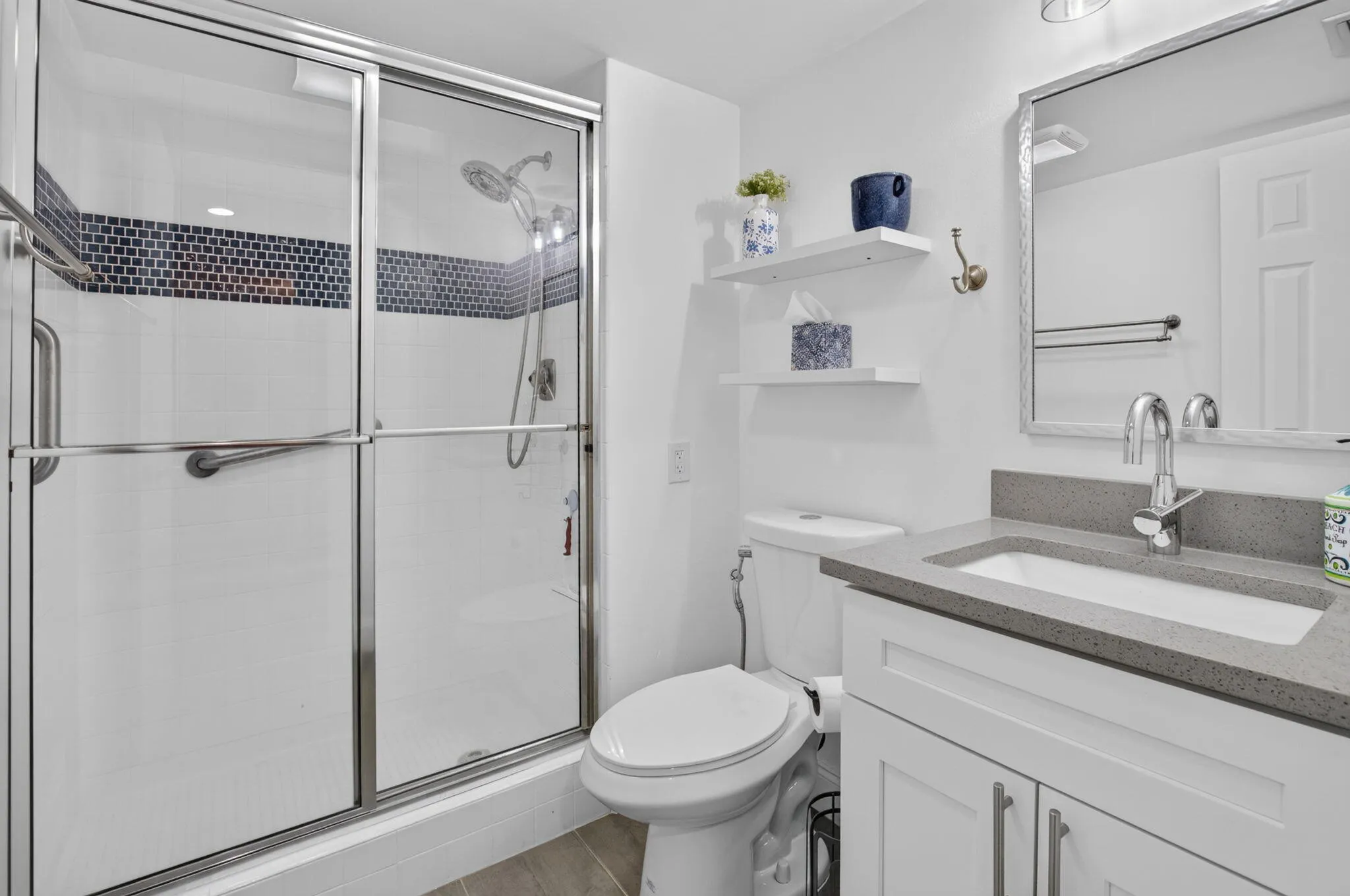 Walk-in shower with sliding glass doors, white tiled walls, and a decorative mosaic accent band