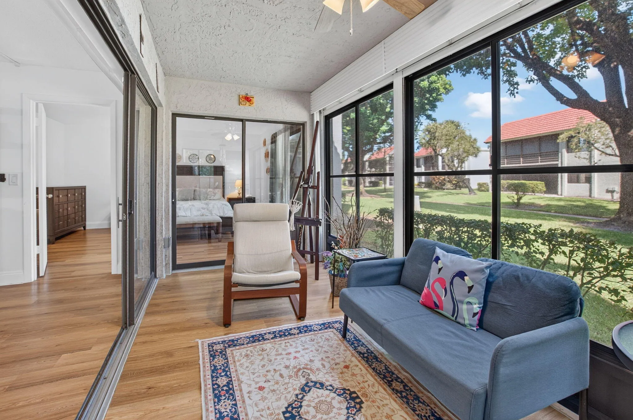 Enclosed Florida room with wood-finish flooring, ceiling fan, and large windows with lush garden views